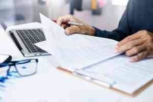 Person mit Dokumenten und Laptop